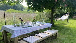 Ein Picknicktisch draußen mit kariertem Tischläufer, Holzbanken und einer Hängematte im Hintergrund.