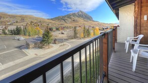 A balcony with a view of a town, a mountain, and a parking lot.