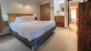 A hotel room with a bed, a nightstand, a desk, a wardrobe, and a bathroom visible through an open door.