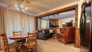 A living room with a dining table, chairs, a sofa, a red armchair, and a kitchen area with a refrigerator.
