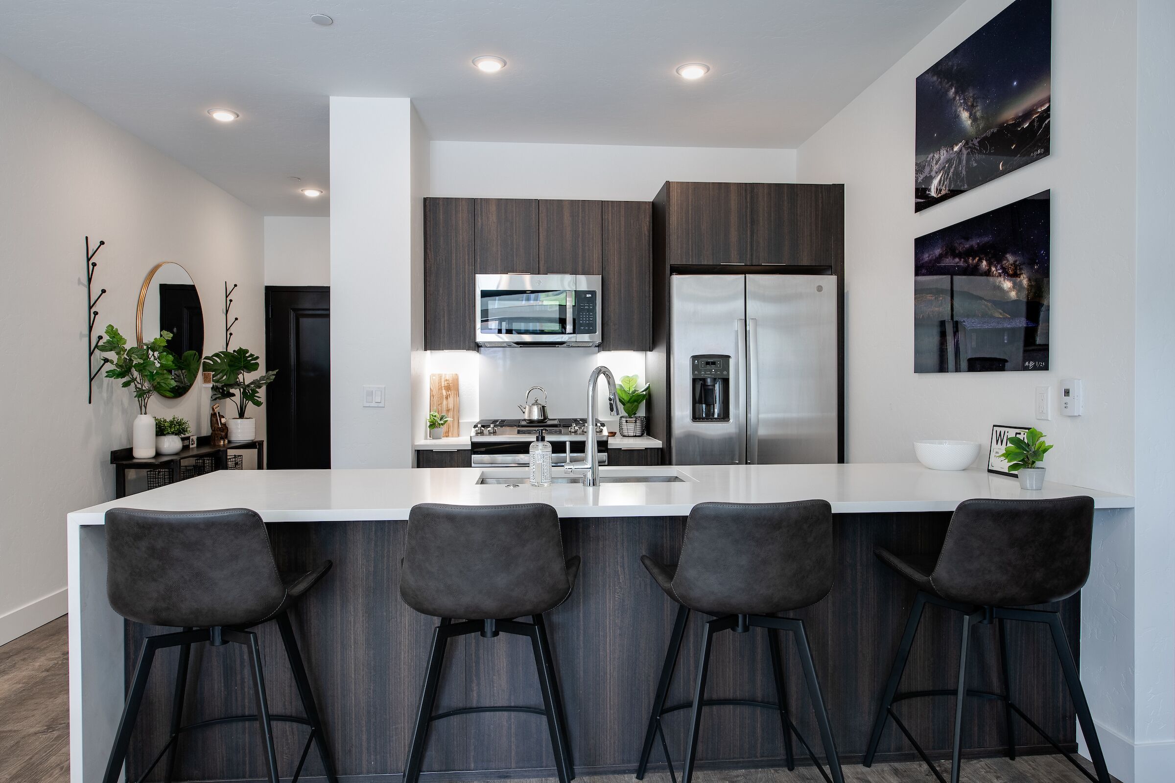 Una cocina moderna con una isla grande, taburetes de bar, un microondas, un refrigerador y dos televisores empotrados.