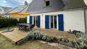 Una casa con terraza de madera, una mesa con sillas y un paraguas amarillo.