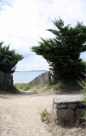 Un sendero arenoso que lleva a una valla de madera, con una estructura de piedra a la derecha.