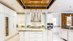 A modern kitchen with white cabinetry, a central island, stainless steel appliances, and a wooden ceiling. - Last Minute Disney Getaway! Private Pool, Hot Tub & Game Room. Book Now! #6266 (Orlando)