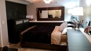 A bedroom with a bed, dresser, mirror, and a desk with a lamp.