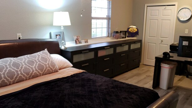 A bedroom with a bed, dresser, desk, and a clock on the wall.