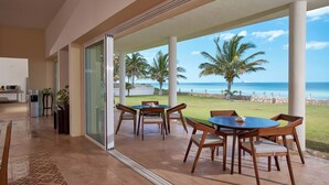 Eine geräumige Terrasse mit Glastür und Blick auf den Strand, ausgestattet mit einem runden Tisch und Stühlen.