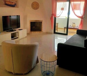 A living room with a flat-screen TV, a fireplace, a sofa, and a dining area with a table and chairs.