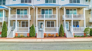 A row of three-story townhouses with balconies, a brick sidewalk, and a clear sky. - Seniors welcome! Large Townhouse near Boardwalk and Beach!! (Ocean City)