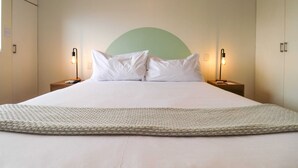 A neatly made bed with white linens and pillows, two bedside lamps, and a large woven throw blanket.