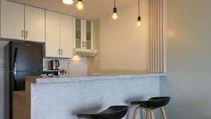 A modern kitchen with white cabinets, a black refrigerator, a countertop, and two black bar stools.