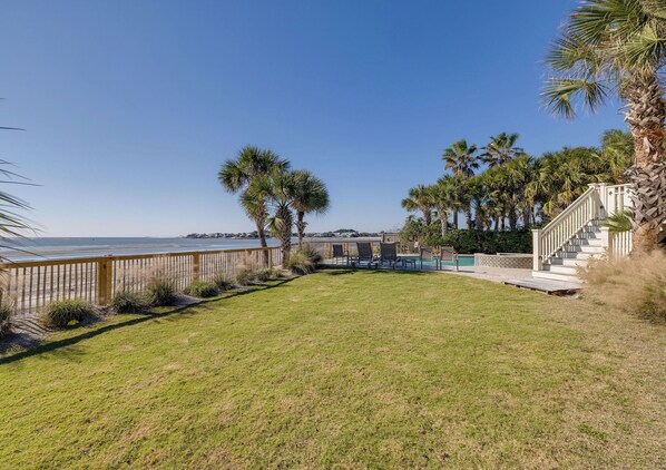 A coastal property with a grassy lawn, palm trees, a wooden fence, and a staircase leading to a building.