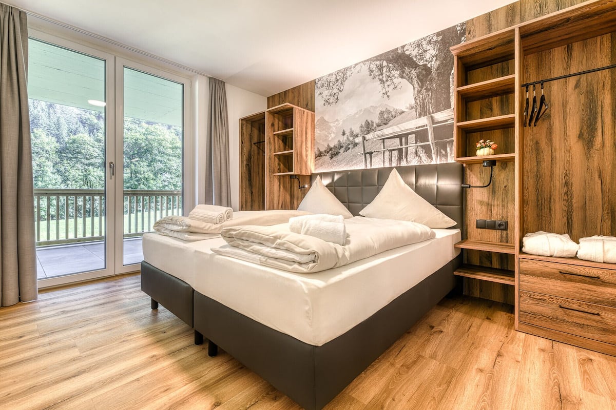 A modern bedroom with a large bed, wooden shelving, and a scenic wall mural.