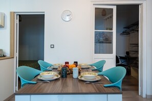 Zona pranzo con tavolo in legno, quattro sedie color turchese e un orologio appeso al muro.