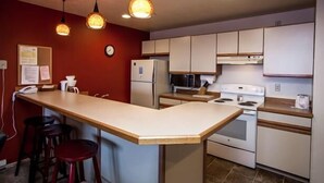 A compact kitchen with a central island, white cabinets, and a red accent wall. - Updated Condo Just a Short Walk to the Slopes (Whitefish)