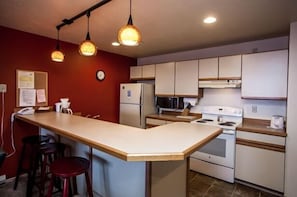 A compact kitchen with a central island, white cabinets, and a red accent wall. - Updated Condo Just a Short Walk to the Slopes (Whitefish)