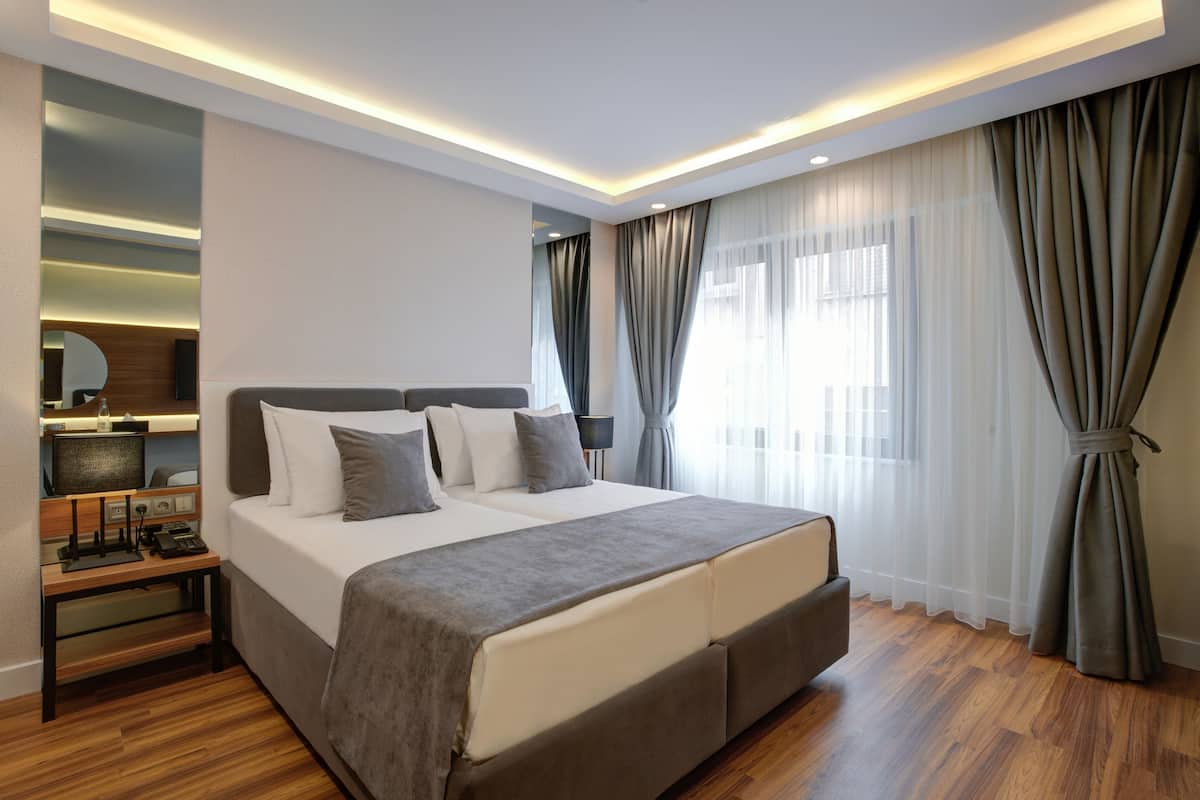A modern hotel room with a large bed, bedside tables, a mirror, and a window with curtains.