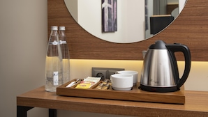 A wooden console table with a round mirror, a stainless steel kettle, a tray with snacks, two water bottles, and a white cup. - Depiero Hotel Karaköy (Istanbul)