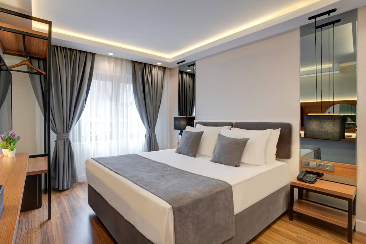A modern hotel room with a large bed, bedside tables, a desk, and a mirror.