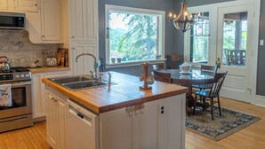 Una cocina con armarios blancos, encimera de madera, horno empotrado y ventana con vistas a un paisaje verde.