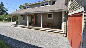 A two-story building with a covered porch, a red garage door, and a gravel driveway. - Phenomenal location in Bath, ME- Comfortable,3 BR, 2 bath, Close to Everything! (Bath)