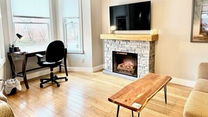 A modern living room with a fireplace, a flat-screen TV mounted above it, and a wooden coffee table. - Phenomenal location in Bath, ME- Comfortable,3 BR, 2 bath, Close to Everything! (Bath)