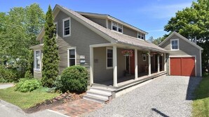 A two-story house with a covered porch, a red garage, and a well-maintained lawn. - Phenomenal location in Bath, ME- Comfortable,3 BR, 2 bath, Close to Everything! (Bath)