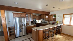 Cocina moderna con armarios de madera, electrodomésticos de acero inoxidable y una isla central con taburetes de bar.