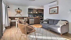 A modern living room with a sofa, a wicker chair, a coffee table, and a kitchen area in the background. - Unique and Sunny Top Floor Old Quebec Gem (Quebec City)