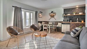 A modern living room with a sofa, two chairs, a dining table, and a kitchen area with a microwave and shelves. - Unique and Sunny Top Floor Old Quebec Gem (Quebec City)