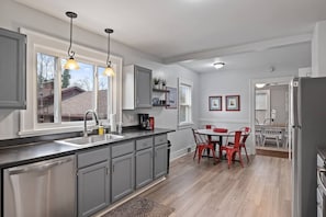A modern kitchen with grey cabinets, a black countertop, and a dining area with red chairs.