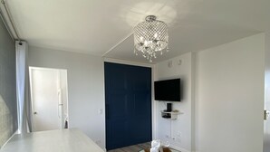 Ein modernes Wohnzimmer mit einem weißen Tisch, einer blauen Tür, einer Kronleuchter und einem an der Wand montierten Flachbildfernseher.
