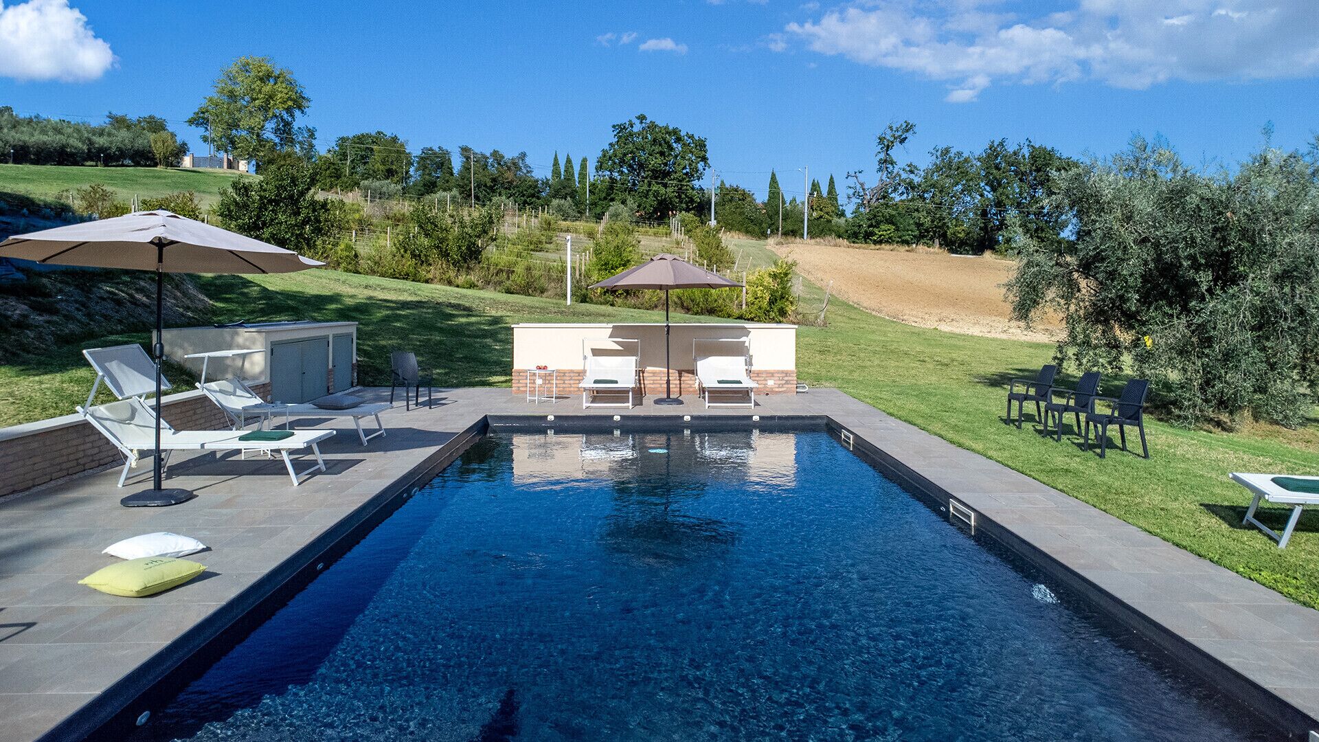 A swimming pool with lounge chairs and umbrellas, surrounded by a landscaped garden.