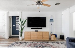 Ein Wohnzimmer mit Flachbildfernseher, Holzschrank, Blumentopf und Teppich mit Muster.