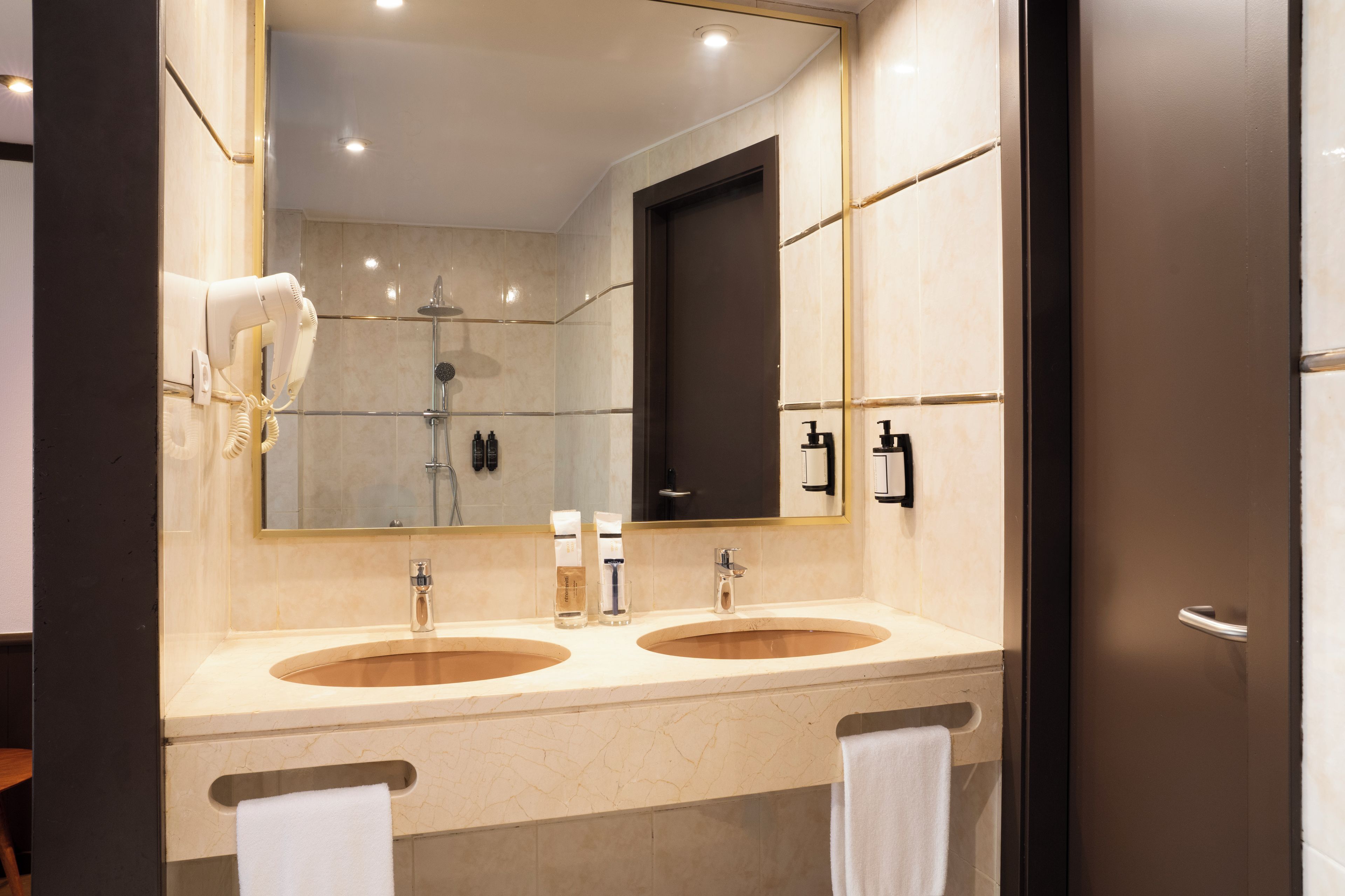 Un baño moderno con dos lavamanos, un espejo grande y un secador de pelo.