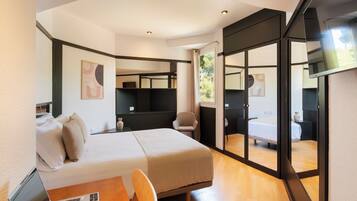 A modern hotel room with a bed, a desk with a laptop, a chair, and a large mirror.