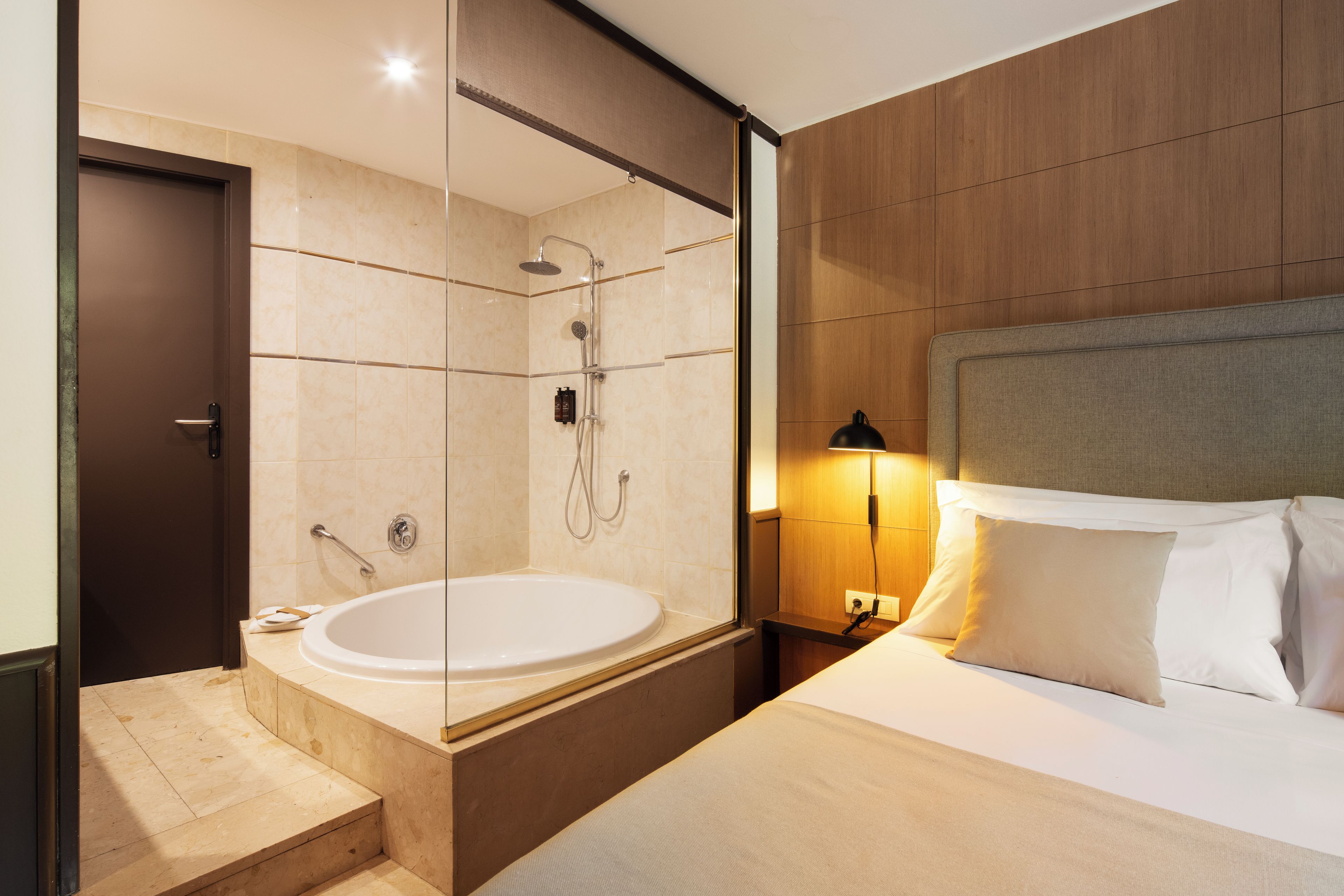 Una habitación de hotel moderna con una cama grande, una zona de ducha separada y una bañera.
