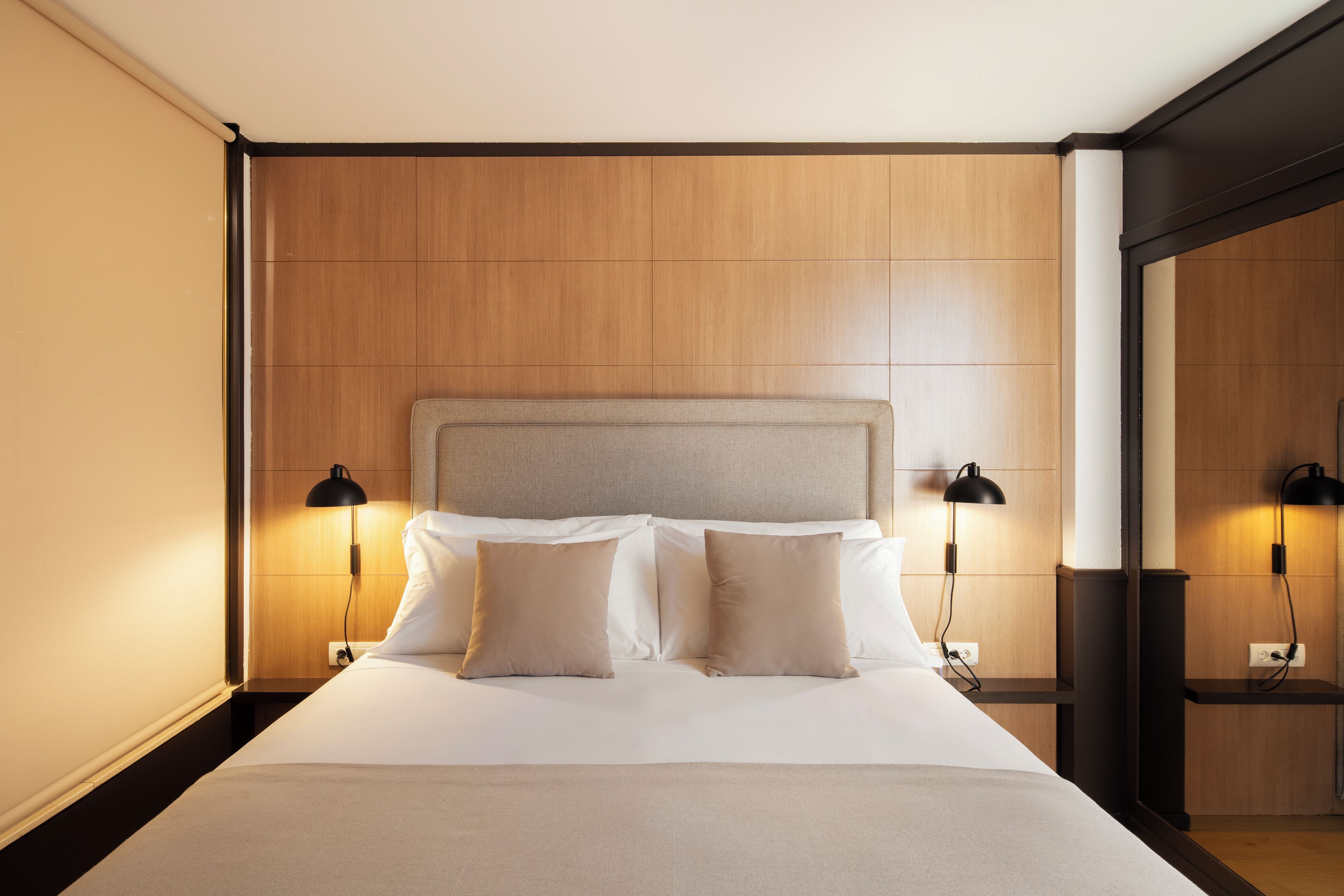 A hotel room with a large bed, two bedside lamps, and a wooden headboard.