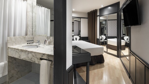 Un baño moderno con lavamanos de mármol, un espejo grande y zona de ducha.