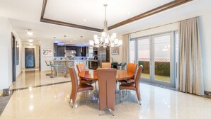 A spacious dining area with a large round table and modern chairs, a chandelier, and a view of the outdoors through large sliding glass doors. - Luxury Beach House for Families - Private Pool, Rooftop & Ocean Views (Fort Lauderdale)