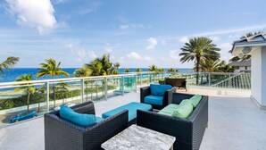 A balcony with wicker furniture, a marble table, and a view of the ocean and palm trees. - Luxury Beach House for Families - Private Pool, Rooftop & Ocean Views (Fort Lauderdale)