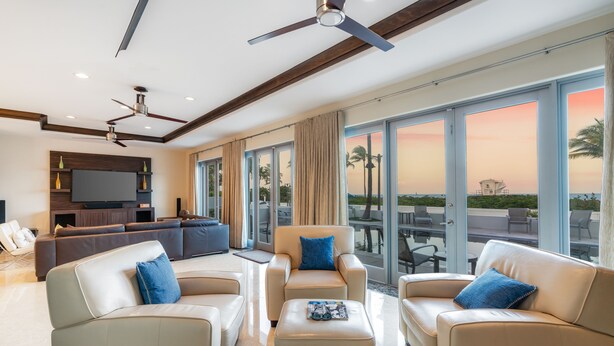 A spacious living room with a large TV, comfortable seating, and a balcony with a view. - Luxury Beach House for Families - Private Pool, Rooftop & Ocean Views (Fort Lauderdale)