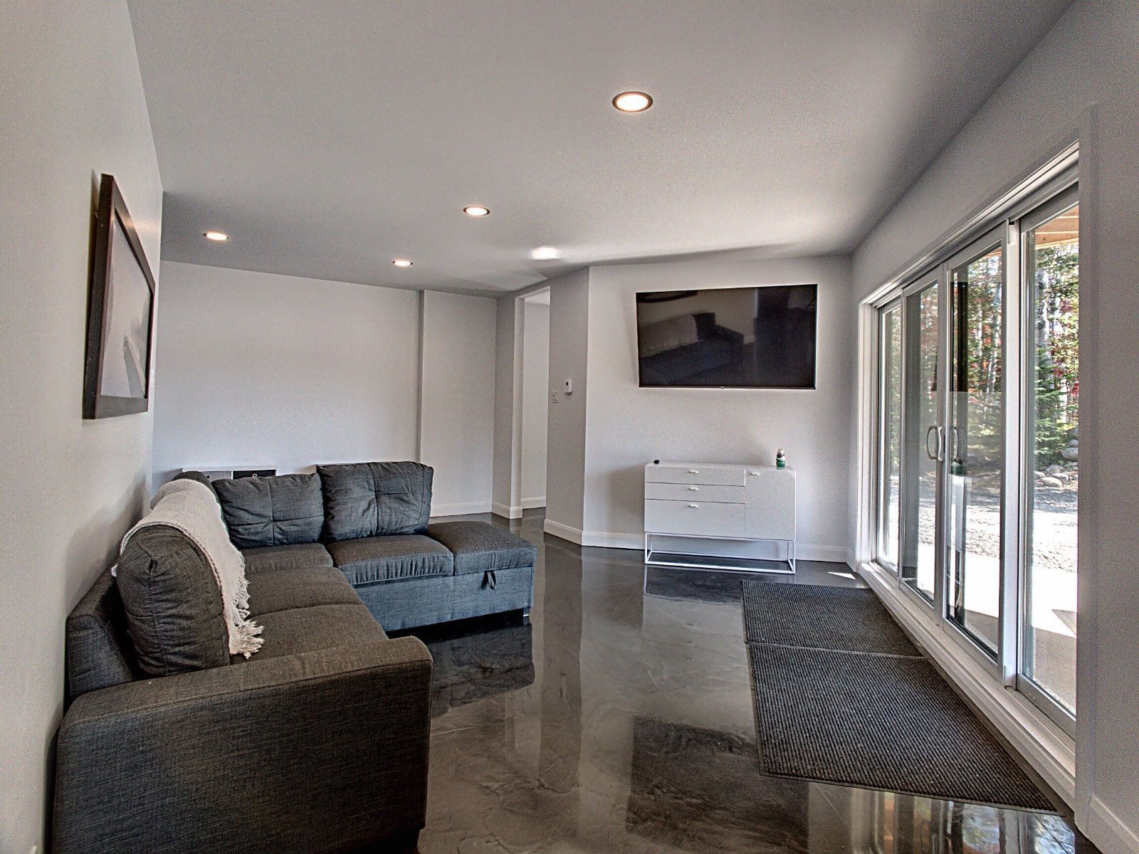A modern living room with a grey sofa, a white cabinet, and a large window offering a view of the outdoors.
