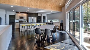 A modern kitchen with a central island, bar stools, and a dining table.