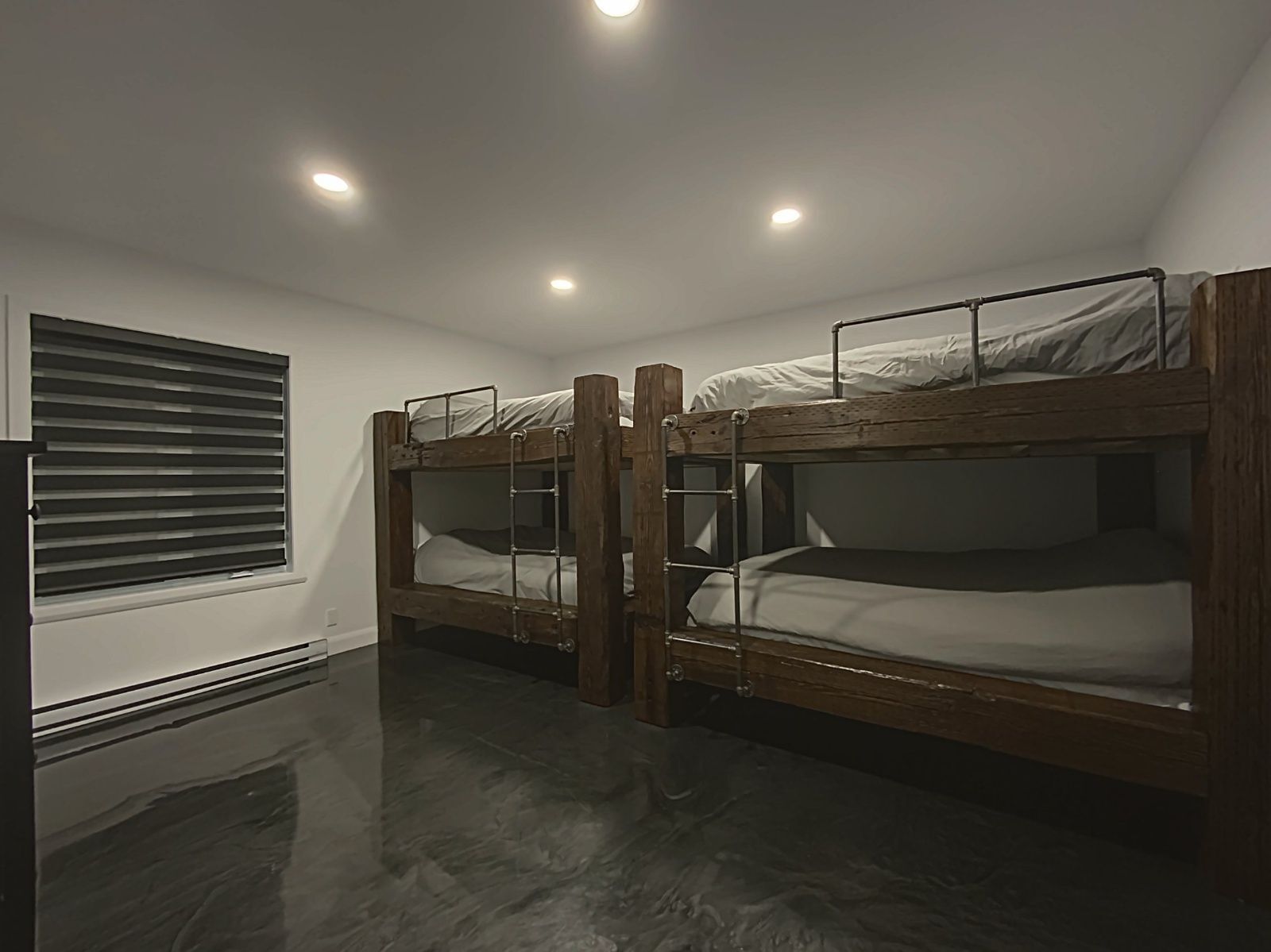 Une chambre avec des lits superposés, une fenêtre avec des stores et un radiateur.
