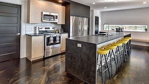 A modern kitchen with a central island, stainless steel appliances, and a bar area with yellow stools.