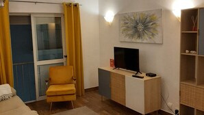 Uma sala de estar moderna com um sofá, uma poltrona amarela, uma TV sobre um móvel de madeira e um quadro na parede.