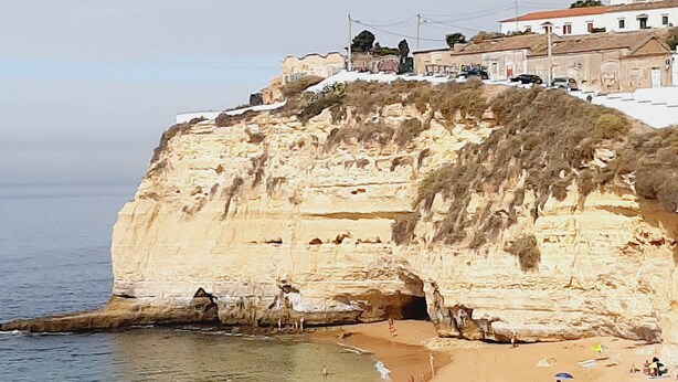 Uma praia costeira com um penhasco e edifícios no topo.