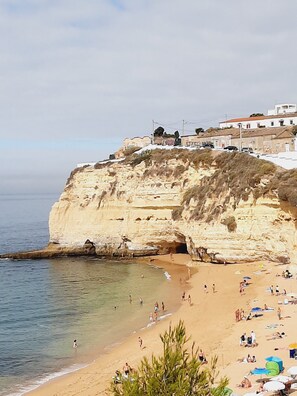 A coastal beach with a cliff and buildings on top. - Cozy apartment 5 minutes to the beach (Carvoeiro)