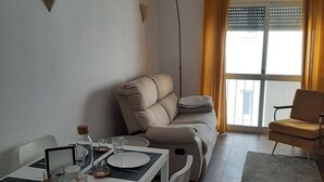 Uma sala de jantar com uma mesa posta para dois, um sofá e uma cadeira.